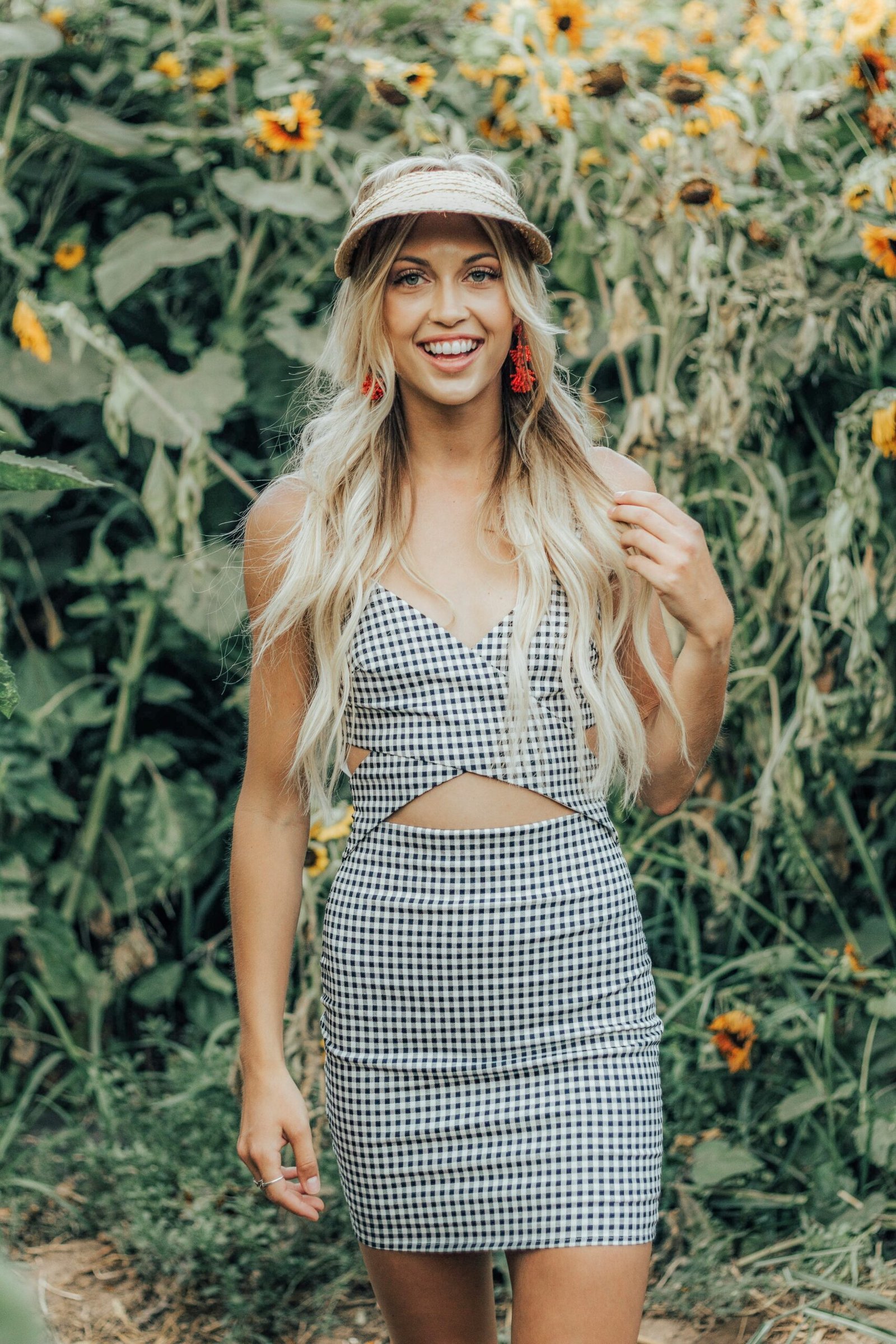 woman in black and gray checked tank dress stands near sunflower